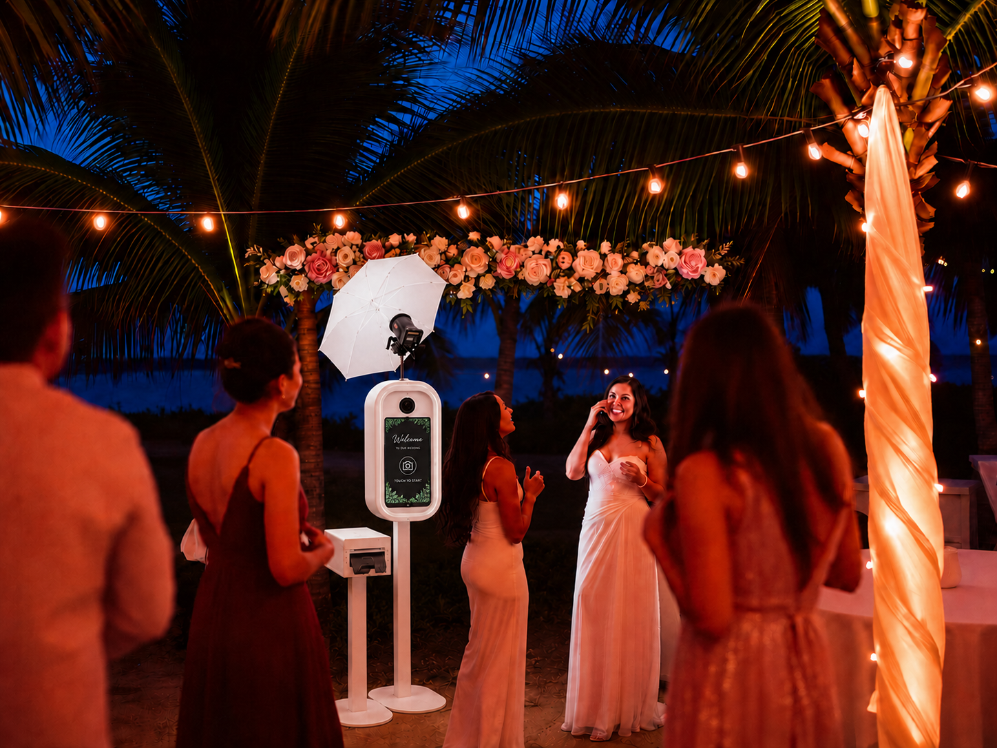 Guests gathered around an open-air photo booth under palm trees and string lights at a Bahamian wedding